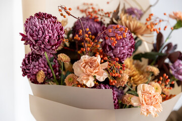 Close-up of a luxurious autumn bouquet featuring textures of purple chrysanthemums, delicate peach carnations, and vibrant orange rowan berries