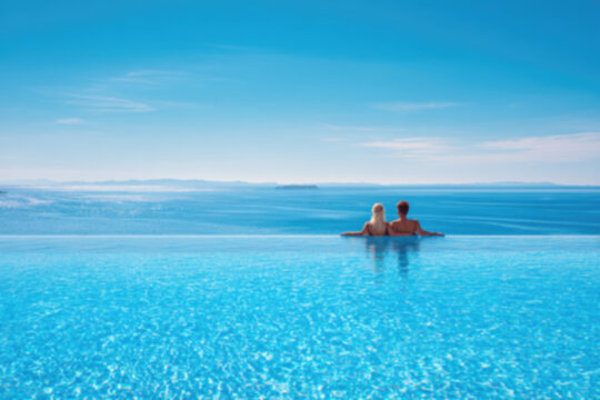 A holiday couple in a big infinity pool enjoys the panoramic view to the blue sea during summer vacation time