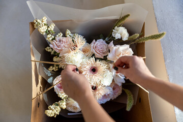 Delicate pastel bouquet with blush pink garden roses, white fringed flowers, and dried accents, carefully packaged in a brown cardboard box for flower delivery.