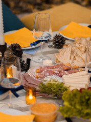 Autumn picnic in the park with a table full of food, pancakes, ham, cheese, and tea. Someone pours sparkling wine into a glass. Cozy setup with candles, fairy lights, pillows, and blankets.
