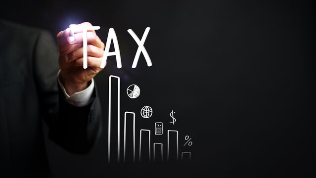 Business professional writing the word tax next to growing financial graphs in a dark setting