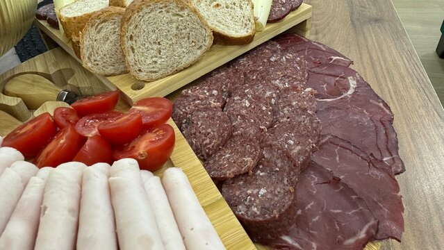 High-quality close-up of a delicious charcuterie board featuring assorted cured meats, sliced turkey/ham rolls, salami, smoked beef, cheese slices, cherry tomatoes, and fresh bread. 