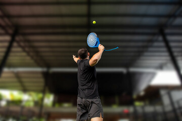 Male player serving a yellow padel ball indoors at a sleek court