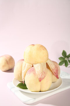 Fresh Yangshan Peaches Arranged on White Plate with Green Leaves on Pink Background