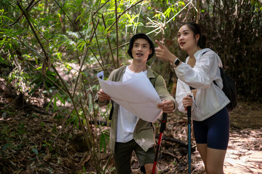 Asian couple hiking forest path navigating with map