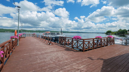 A wooden pier on Lake Żarnowieckie. Pink surfinias hang from the railing. A beautiful summer day. Nadole, Kashubia, Poland