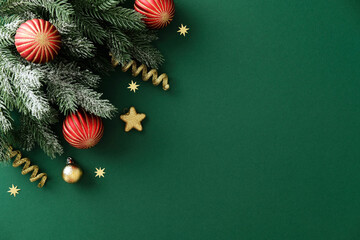Christmas green background with snowy pine branches, red and gold baubles, and confetti stars. Flat lay, top view, copy space.