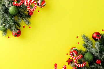 Bright Christmas background with copy space. Vibrant yellow background with lush green spruce branches dusted with snow, decorated with red and green baubles, candy canes, and red stars