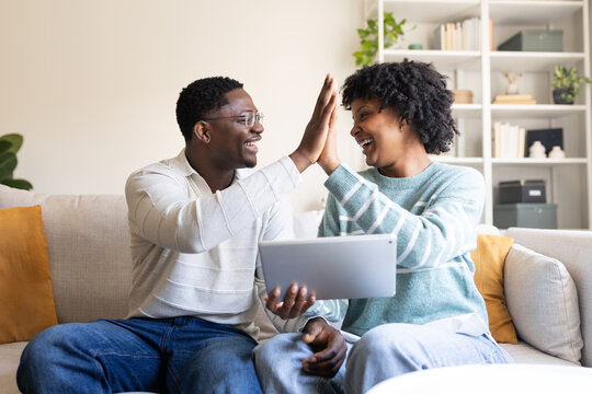 Happy couple giving high five celebrating success using digital tablet at home