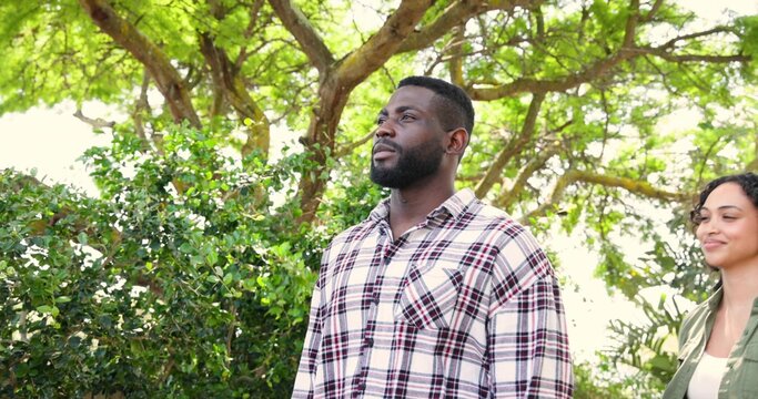 Standing bearded man gazing upward at park trees, showing plaid shirt, woman in green jacket