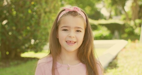 Smiling girl wearing light pink ribbed top showing missing front tooth in garden, pink headband
