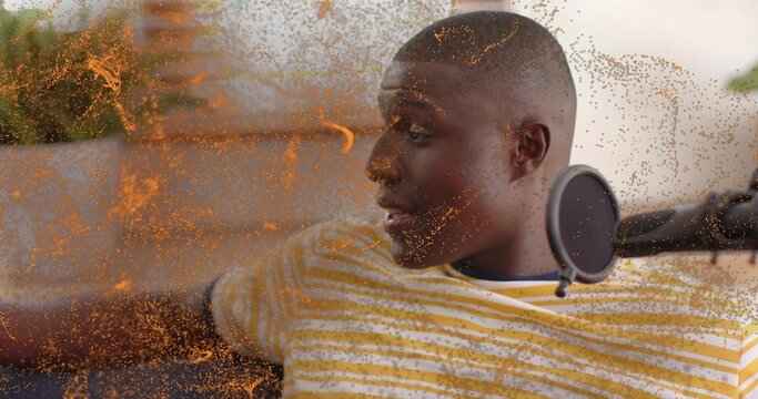 Reclining man in yellow striped tee recording on sofa at home, with mic and pop-filter, orange-dust