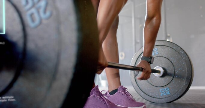 Gripping female lower body and hands preparing to lift loaded barbell on gym floor, purple shoes