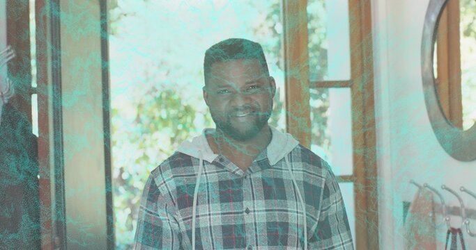 Smiling man standing in entryway, wooden glass door, mirror, wall hooks, plaid hoodie, teal overlay - Powered by Adobe
