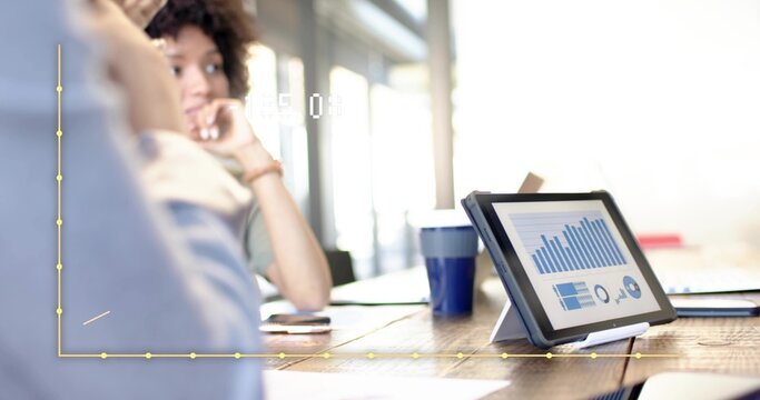 Displaying tablet on stand at meeting table, colleagues in blue shirt discussing charts, copy space