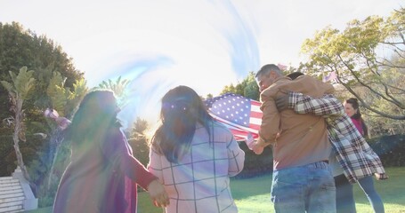 Linking arms, six adults walking on grassy lawn, holding American flag, wearing coats and jeans