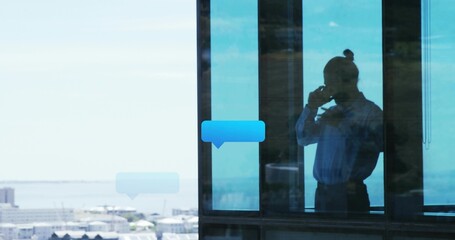 Talking male in shirt holding smartphone by glass in office with blue speech-bubbles, copy space