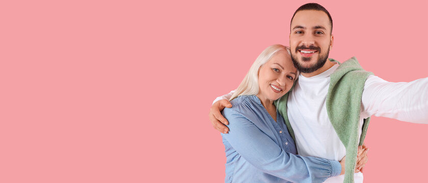Young man hugging his mother and taking selfie on pink background