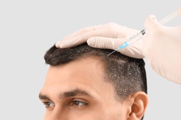 Naklejka premium Young man with dandruff receiving injection from trichologist on light background, closeup