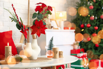 Vase with Christmas flower poinsettia and burning candles on table in living room