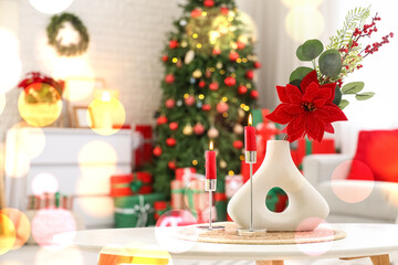 Vase with Christmas flower poinsettia and burning candles on table in living room
