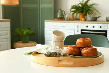 Dining table with cinnamon rolls, tea leaves and cups in modern kitchen