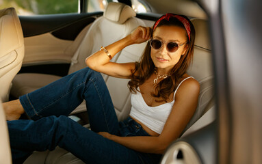 Relaxed woman reclining with legs up in car backseat, casual denim and bandana, sunlit interior offering calm weekend commute