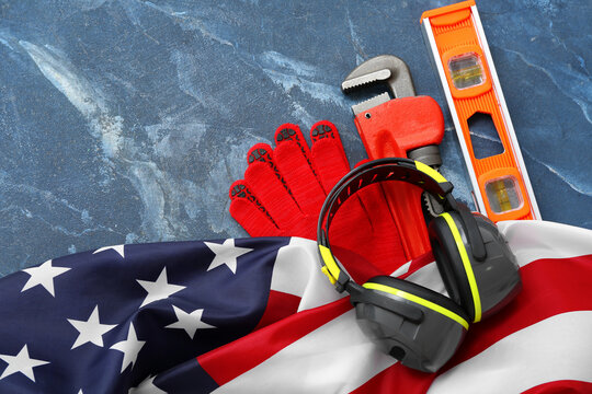 Earmuffs, pipe wrench, gloves and USA flag on blue table. Labor Day celebration