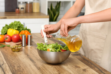 Woman adding olive oil into bowl with tasty salad at table in kitchen
