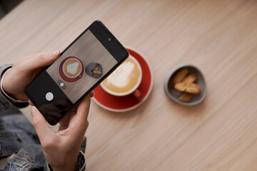 Person taking cell phone picture of latte art coffee