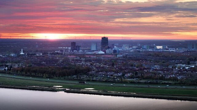 Almere, Netherlands at sunrise, with vibrant clouds, city skyline, illuminated water, and gentle morning traffic, capturing tranquil urban awakening and the colorful sky transition.