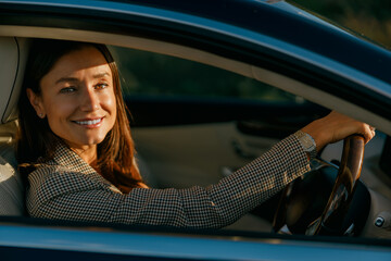 smiling woman behind wheel poised for client meeting, business-casual blazer, hands on steering wheel, attentive gaze, warm