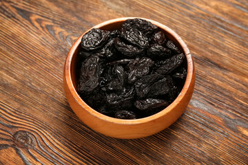 Bowl with tasty dried plums on wooden background