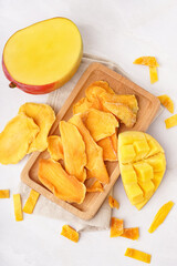 Wooden board with slices of dried mango on white background