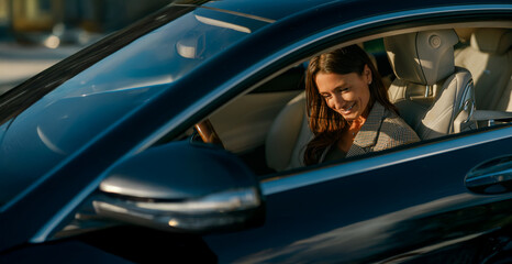 Woman laughing while parked in car, sunlight catching smile as she checks phone, relaxed posture and candid expression convey