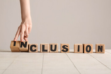 Female hand making word INCLUSION from wooden cubes on white tiled table