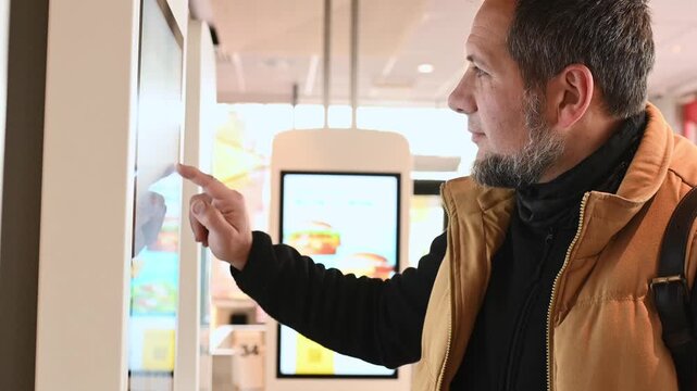 Man using self-service touchscreen kiosk in modern restaurant, interacting with digital ordering system, choosing items on interactive display, concept of technology, automation, and customer convenie