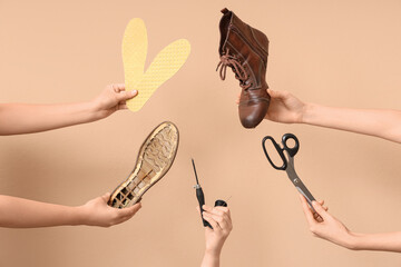 Female hands with shoe pieces, craft tools and insoles on beige background. Shoes repair concept