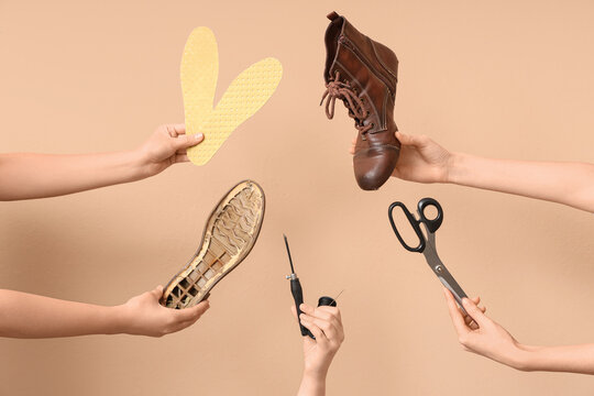 Female hands with shoe pieces, craft tools and insoles on beige background. Shoes repair concept