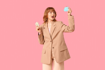 Beautiful young woman holding money and blue purse on pink background