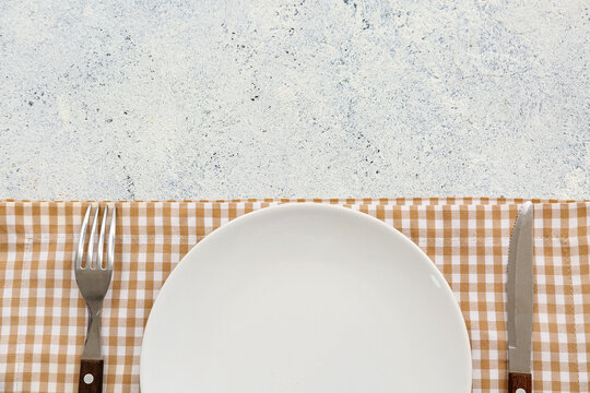 Table setting with plate, cutlery and napkin on white grunge background