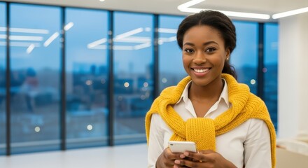Young African American woman smiling and holding a smartphone in a modern office building 
