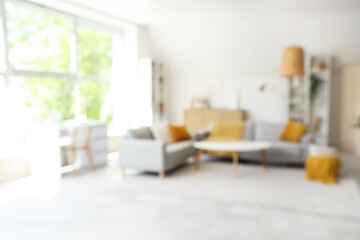 Blurred view of light living room with grey sofas, table and shelf units