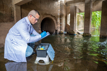 Scientist Taking Environmental Water Sample with plastic glass and Protective Gear Near Drainage Tunnel