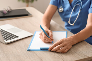 Fototapeta premium Mature female doctor writing on clipboard at table in clinic, closeup