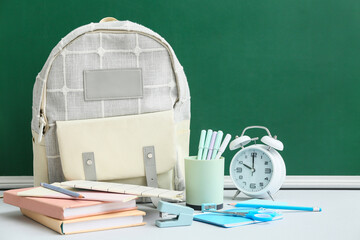School backpack with different stationery supplies and alarm clock on white table