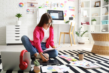 Female graphic designer working with tablet on floor in office