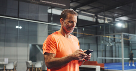 Sport practice, man and happy with phone for padel training schedule, court booking or research. Tennis player, mature person and smile with smartphone at indoor club for fitness app and track score