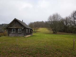Old wooden house in a grassy field surrounded by trees  