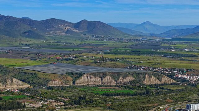Aerial telephoto view of plantations with protective nets in the Limar&iacute; Valley with green mountains on a sunny day. Plantations for Chilean pisco.